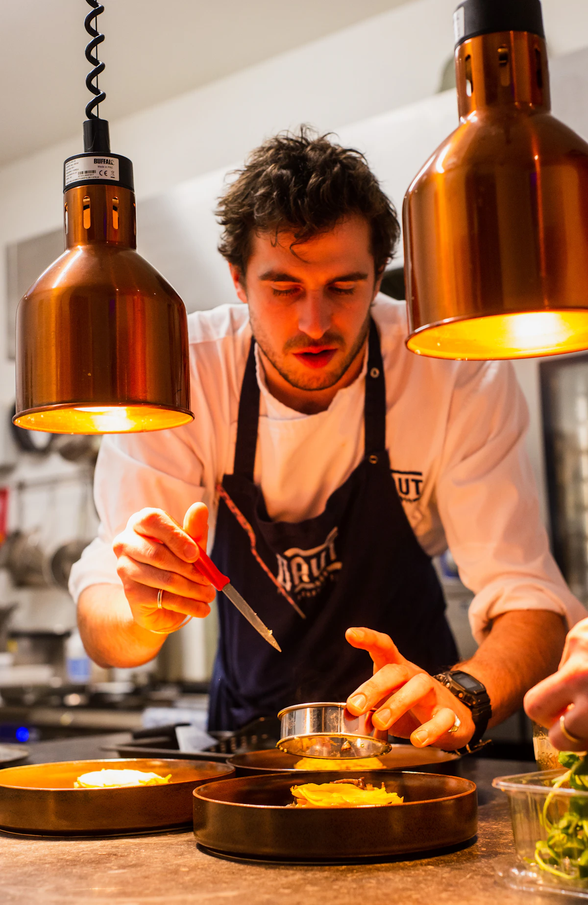 Chef finalizando cuidadosamente um prato sob a luz quente da cozinha