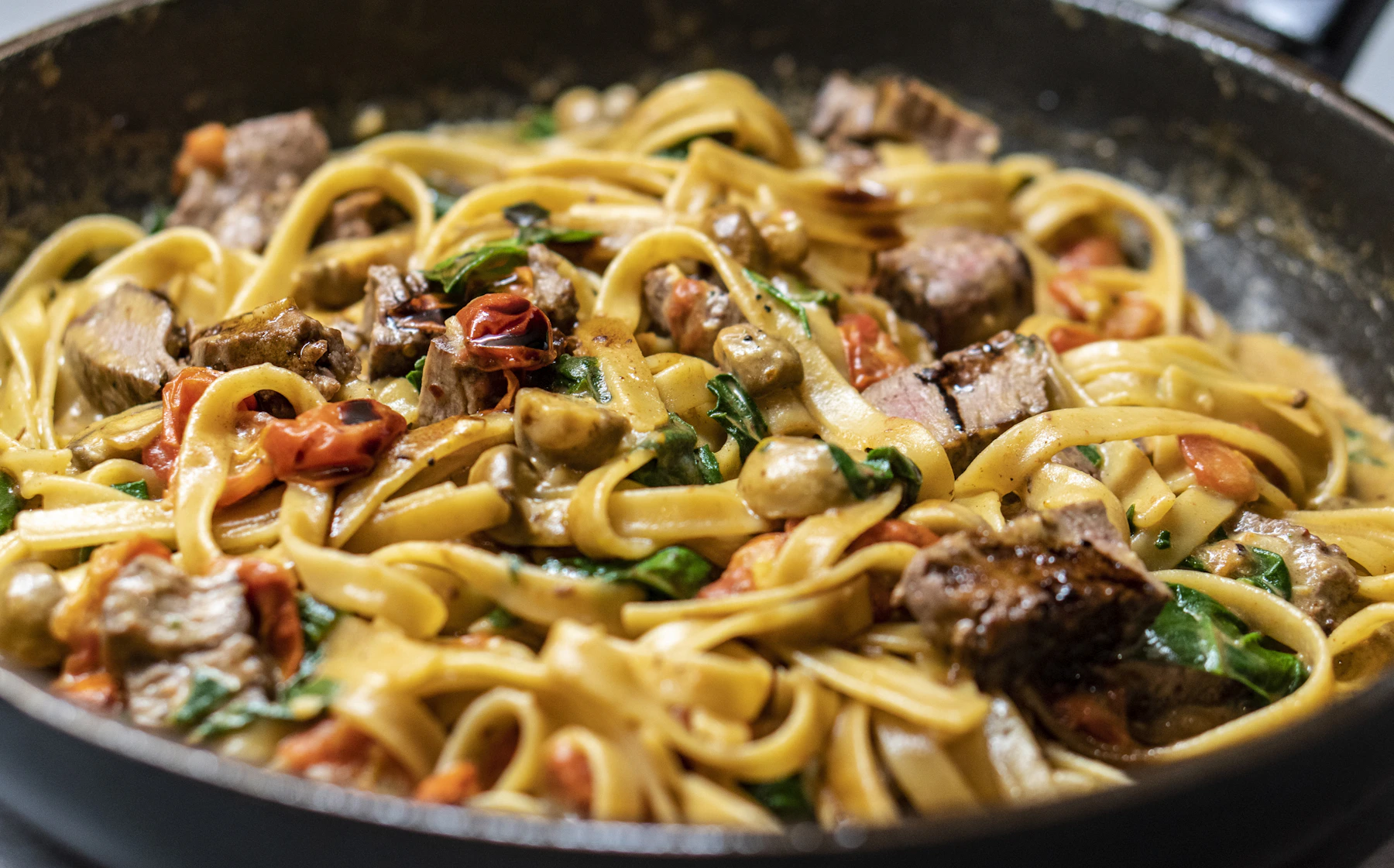 Tagliatelle com filé, tomates e ervas em panela escura